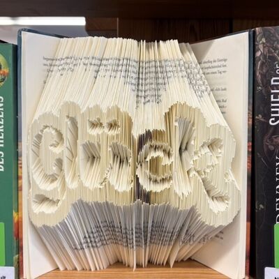 Ein offenes Buch, bei dem durch Faltung der Seiten ein visuelles Wort entsteht. 